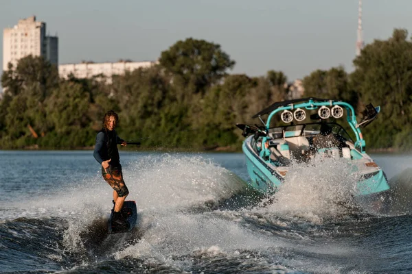 Bateau à moteur lumineux tire un homme actif chevauchant un wakeboard et montrant geste de surfeur — Photo