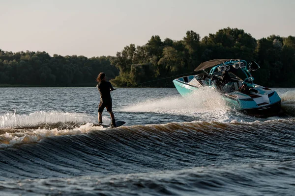 Heldere motorboot trekt een actieve man op een wakeboard langs de rivier — Stockfoto