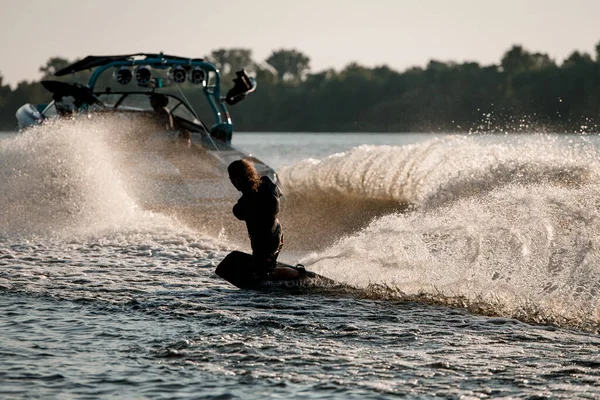Homme athlétique tient la corde et équilibrage sur wakeboard derrière bateau à moteur sur éclaboussures vagues de rivière. — Photo