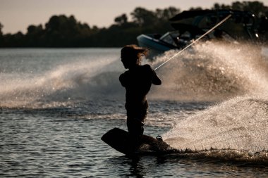Wakeboardcu gergin halatı tutar ve su sıçratan dalgaların üzerinde durmaya çalışır..