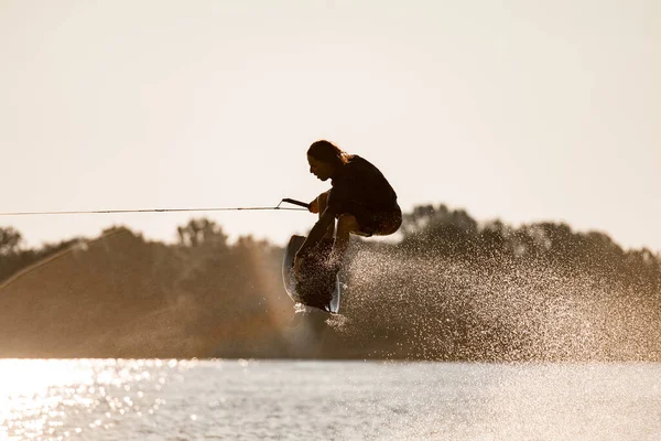 Widok z bliska na faceta trzymającego linę i umiejętnie skaczącego wysoko z wakeboardem nad wodą — Zdjęcie stockowe