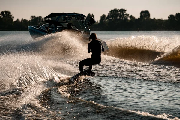 Hátsó kilátás energia ember lovaglás wakeboard mögött motorcsónak fröccsenő folyóhullámok. Aktív és extrém sportok — Stock Fotó