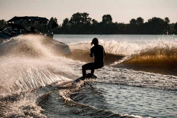 Vue arrière de l'homme chevauchant wakeboard derrière bateau à moteur sur éclaboussures vagues de rivière. Sports actifs et extrêmes — Photo