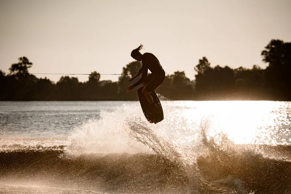 Wakeboarder masculino magistralmente pulando no wakeboard sobre onda salpicando — Fotografia de Stock