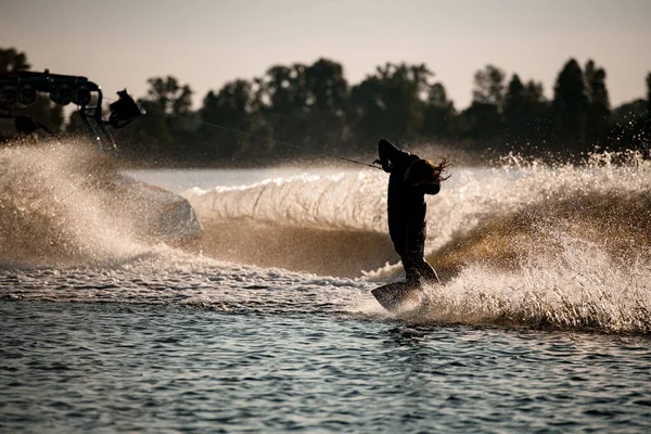 Homme tenant la corde et faisant tour wakeboard équitation derrière bateau à moteur sur éclaboussures vagues. — Photo