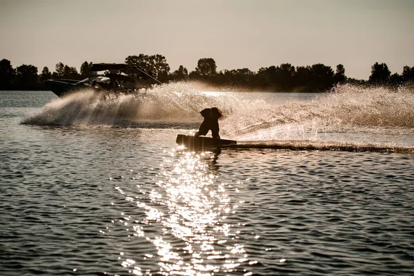 Energie man houden touw en rijden wakeboard en het maken van truc achter de motor boot op spetterende rivier golven. — Stockfoto