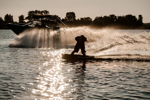 Energia ember kezében kötél és lovaglás wakeboard és ügyesen, hogy trükk mögött motorcsónak fröccsenő folyó hullámok. — Stock Fotó