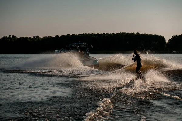 Nagy hátsó kilátás energia ember lovaglás wakeboard mögött motorcsónak fröccsenő folyóhullámok. Aktív és extrém sportok — Stock Fotó