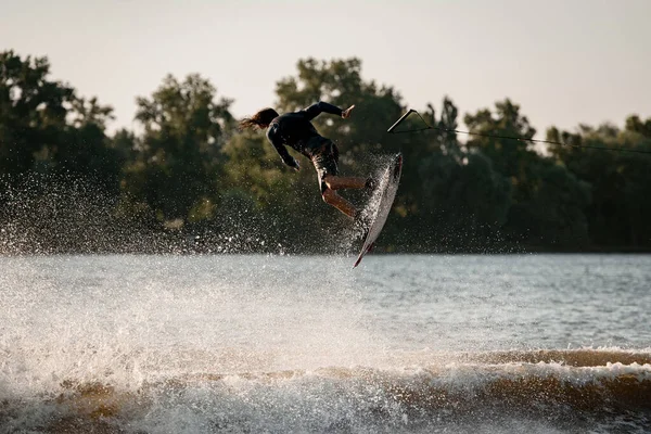 Hombre activo haciendo truco en el tiempo de salto con wakeboard y muchos salpicaduras alrededor —  Fotos de Stock
