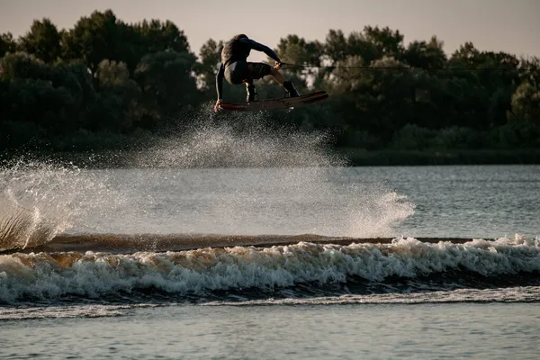 Vue magnifique du gars dynamique tenant la corde et sautant haut avec wakeboard sur l'eau — Photo