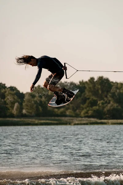 active man holding rope and making trick in jump time with wakeboard over water