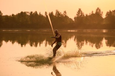 Gülümseyen atletik kaslı adam halatı tutuyor ve wakeboard sürüyor.