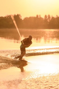 Yetişkin sporcu adam halatın sapını tutuyor ve suda bir wakeboard ile ustaca dengeliyor.