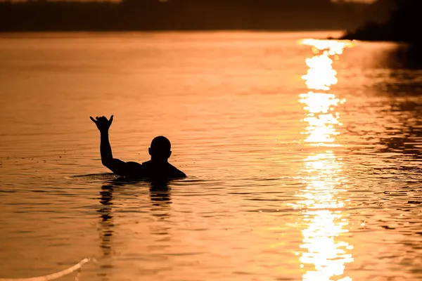 Silueta de un hombre en el agua muestra el gesto de la mano shaka —  Fotos de Stock