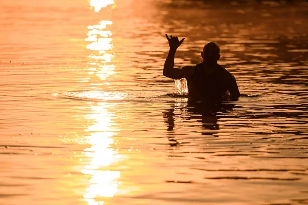 Красивий вечірній вигляд чоловіка у воді, який показує жест руки шака — стокове фото