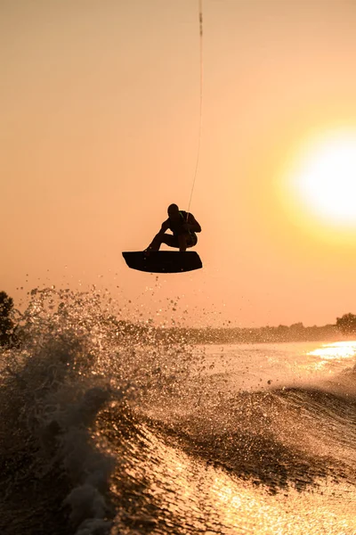 Silueta del hombre activo haciendo truco con wakeboard en el cielo naranja brillante y el fondo del sol. —  Fotos de Stock