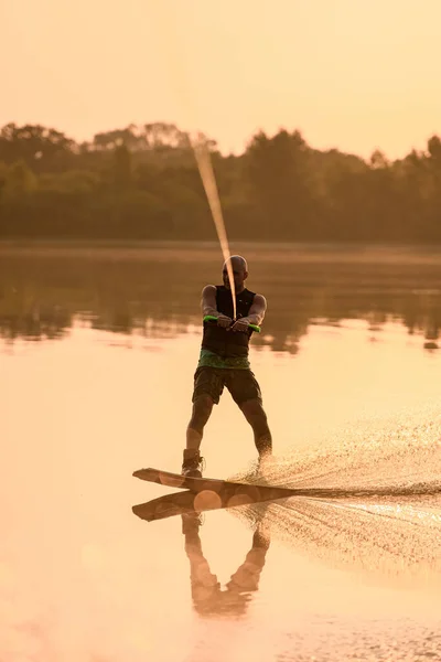 Homem atlético envolvido em esporte aquático e habilmente equilibrando na superfície da água em um wakeboard — Fotografia de Stock