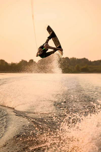 Amazing view of active strong male rider holds rope and making extreme jump showing trick with wakeboard. — Stock Photo, Image