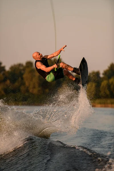 Uomo forte attivo tiene la corda e fare salto estremo mostrando trucco con wakeboard. — Foto Stock