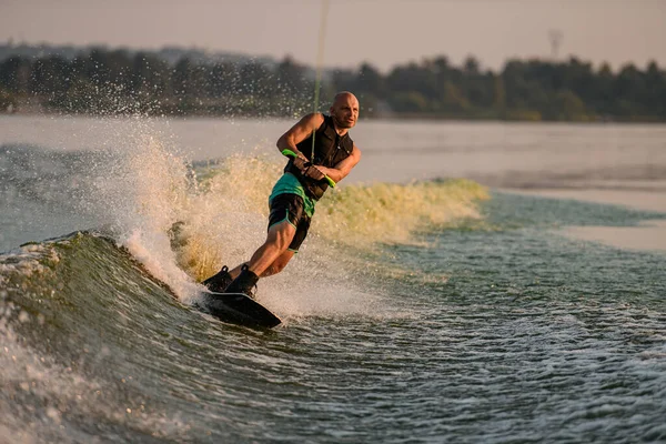 Atletik kaslı adam ipi tutuyor ve akan nehir suyunda enerji dolu bir şekilde wakeboard sürüyor.. — Stok fotoğraf