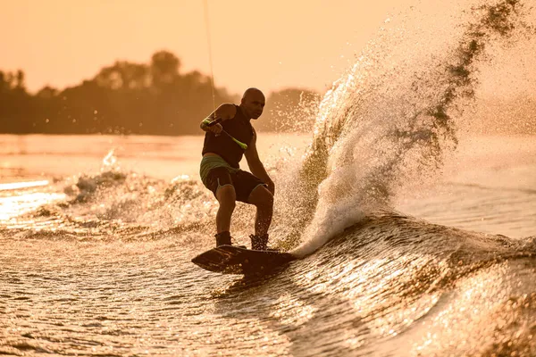 Tolle Aussicht auf plätschernde Welle und athletischen Mann, der energisch Wakeboard fährt. — Stockfoto