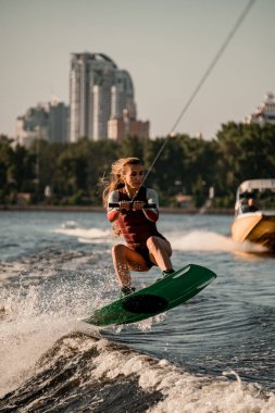 Güzel aktif kadın halat tutuyor ve Wakeboard 'la nehir dalgasının üzerinden atlıyor..