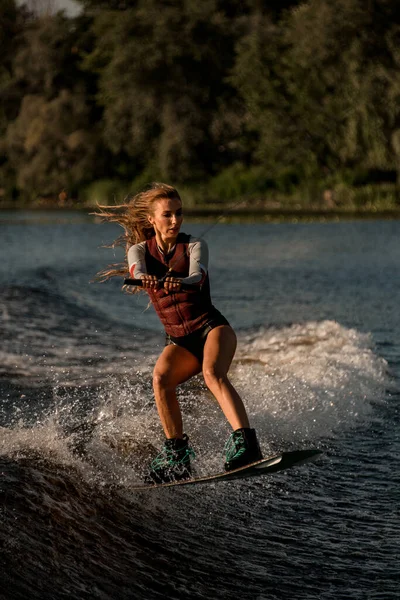 Bello donna tiene corda e saltando con wakeboard oltre fiume onda. — Foto Stock