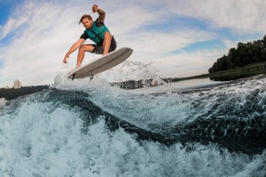 Enerjik erkek wakeboardcu numaralar yapıyor ve akan nehir dalgalarının üzerinden atlıyor