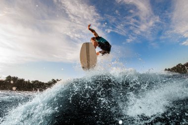 Enerji erkek wakeboardcu nehir kıyısındaki yüksek dalgaları kullanarak atlamada hile yapıyor.