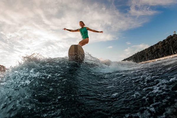 Femme souriante s'amusant wakesurf sur la planche sur la vague de la rivière contre le ciel bleu — Photo