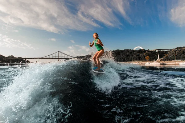 Femme gaie sur wakeboard activement chevauchant la vague de la rivière et montrer geste de la main — Photo