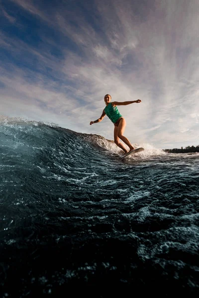 Wakesurfer femelle chevauchant vigoureusement sur wakeboard sur les vagues de la rivière contre le ciel bleu. — Photo