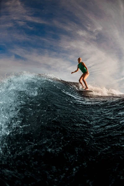 Donna attiva wakesurfer cavalcando sul wakeboard lungo le onde del fiume contro il cielo blu. — Foto Stock