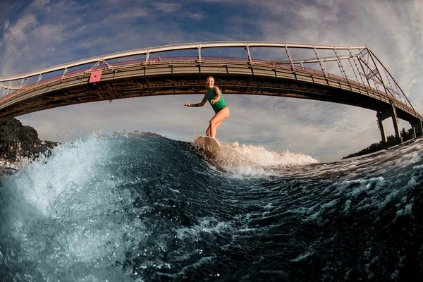 Fantastisk utsikt över kvinnan väckarklocka rider ner på brädet på stänk våg mot bro. — Stockfoto