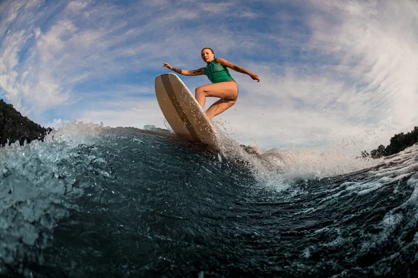 Aktiva kvinnliga väckare hoppar på en wake board på stänk flod våg mot himlen — Stockfoto