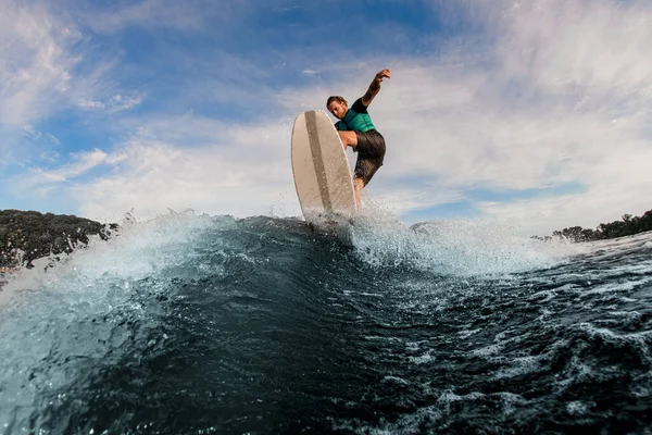 Wakesurfer attivo che salta su un asse di veglia su onda fluviale spruzzante contro cielo — Foto Stock