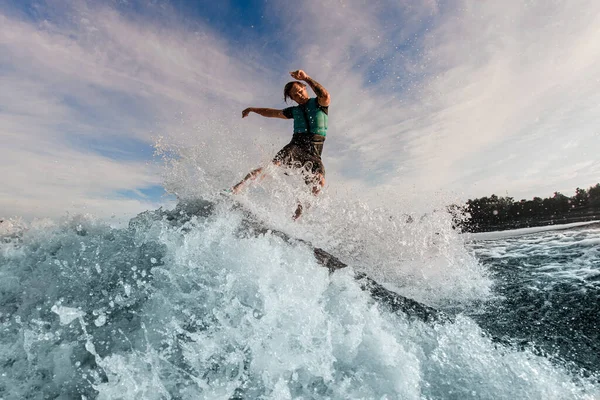 Hombre enérgico wakesurfer montar por la ola salpicadura azul en un día cálido —  Fotos de Stock