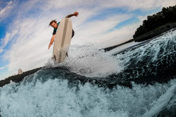 Tipo activo wakesurfer saltando en una tabla wakesurf sobre salpicaduras de olas del río —  Fotos de Stock