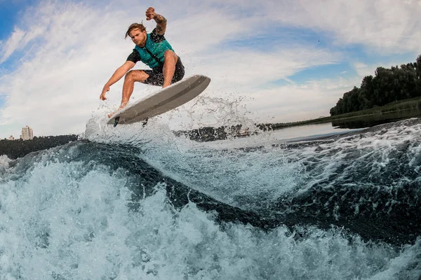 Energía masculina wakeboarder realiza trucos y saltar sobre salpicaduras ola del río —  Fotos de Stock