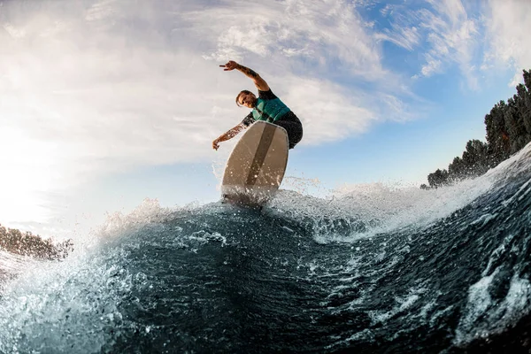 Vista de um atleta do sexo masculino pulando com um wakeboard sobre uma onda salpicante — Fotografia de Stock