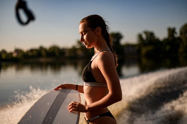 Vue latérale d'une belle femme en maillot de bain tenant une planche de wakesurf — Photo