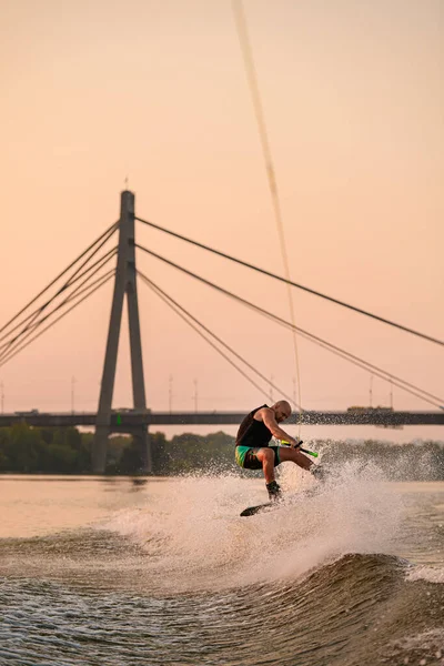 Energia uomo tiene corda e salta abilmente sul wakeboard su sfondo ponte della città. — Foto Stock