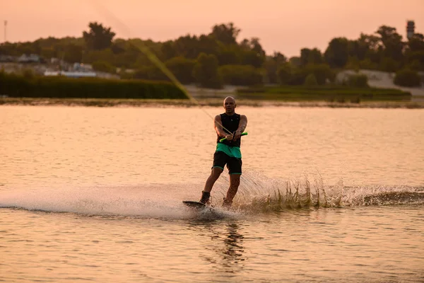 Forte uomo atletico tiene corda e wakeboard equitazione sulla superficie dell'acqua. — Foto Stock