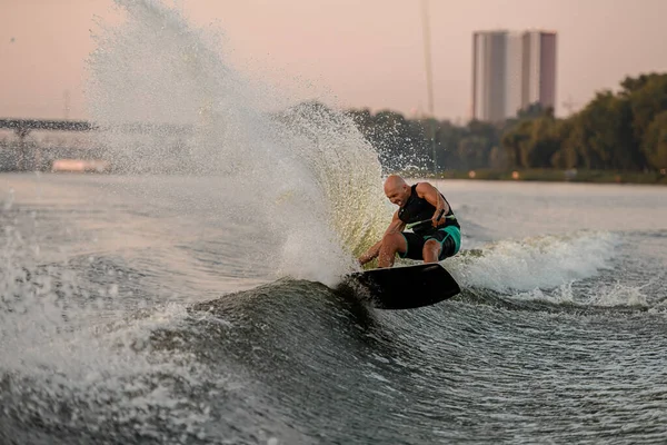 Uomo di energia che cerca di stare in piedi su un'onda spruzzante su un wakeboard — Foto Stock