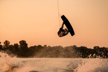güçlü bir adam atlama zamanında günbatımında gökyüzü arka planında wakeboard ile numara yapıyor..