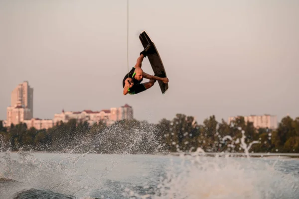 Athlétique gars fort tient la corde et sautant énergiquement et flip avec wakeboard. — Photo