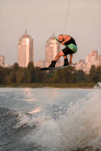 L'uomo attivo tiene la corda e salta abilmente in alto sul wakeboard sopra spruzzi d'acqua. — Foto Stock