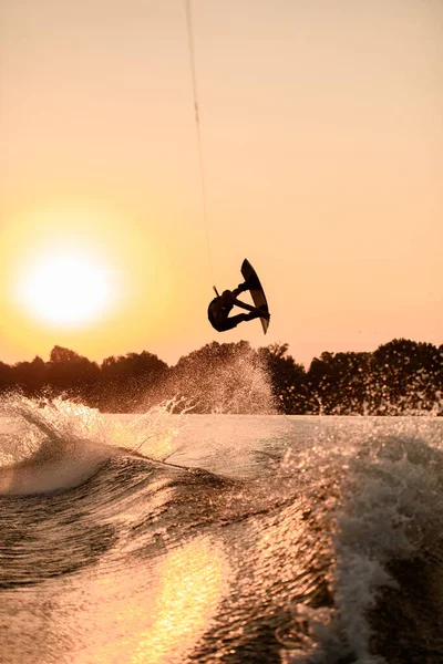 Belle silhouette sombre de l'homme tenant la corde et faisant sauter sur wakeboard au coucher du soleil. — Photo