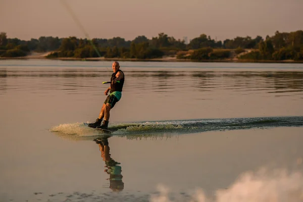 Ottima vista dell'uomo muscoloso che tiene la maniglia con cavo e rotoli sull'acqua sul wakeboard — Foto Stock