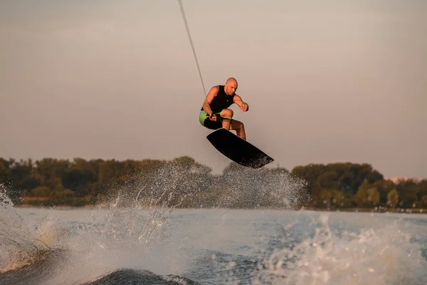 Muskulös man håller kabel och skickligt hoppa över stänk våg på wakeboard. — Stockfoto